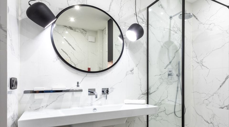 Salle de bains rénovée : carrelage effet marbre, miroir rond, vasque suspendue et douche à l'italienne